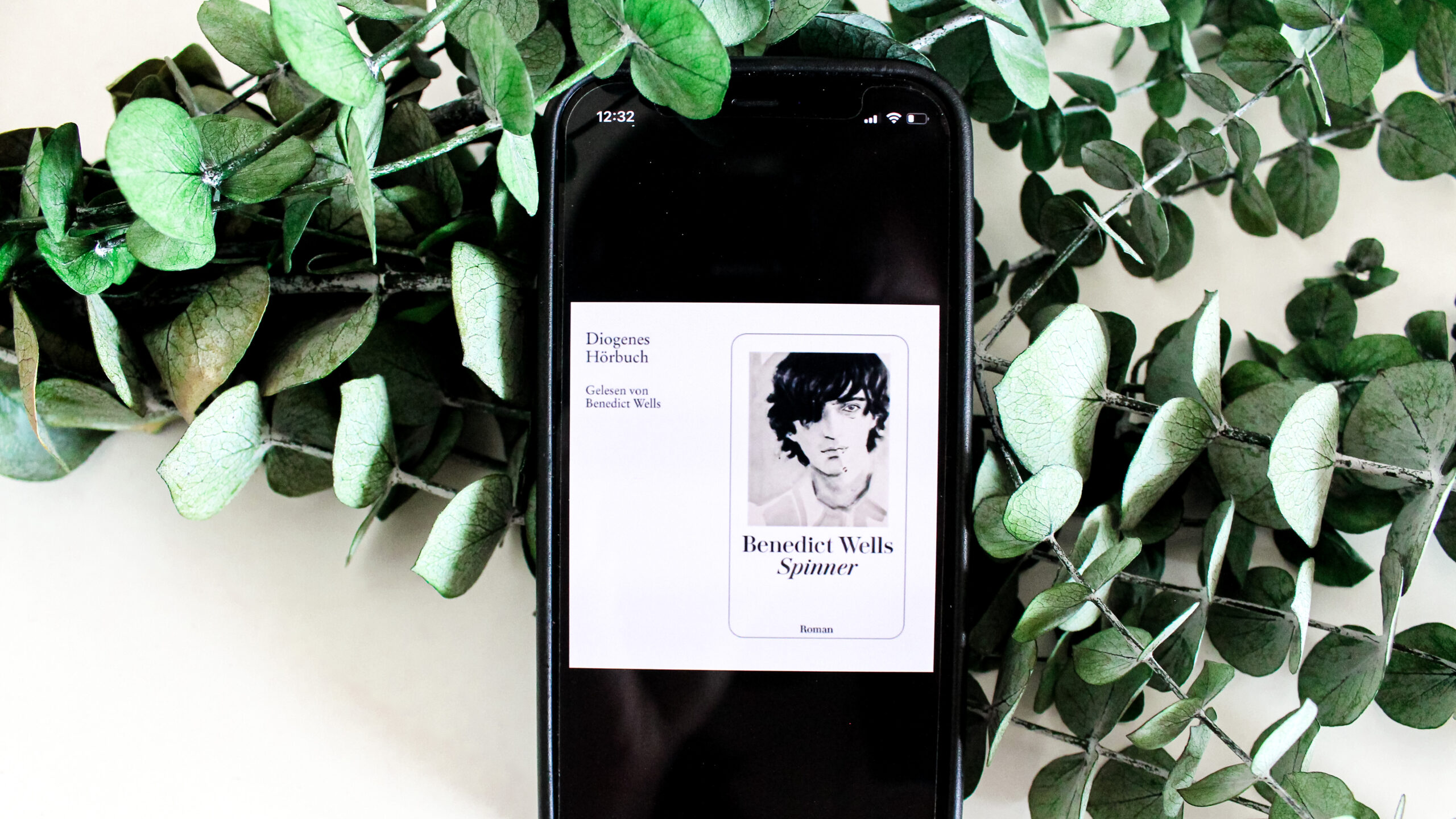 Smartphone Screen zeigt Hörbuchcover von Spinner von Autor Benedict Wellt vor Eucalyptuszweigen